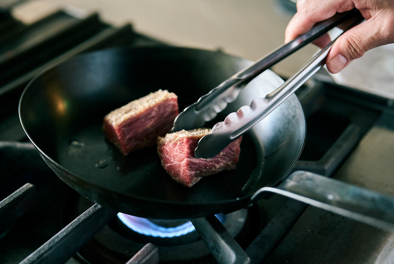 トングを使いフライパンで肉を焼いている