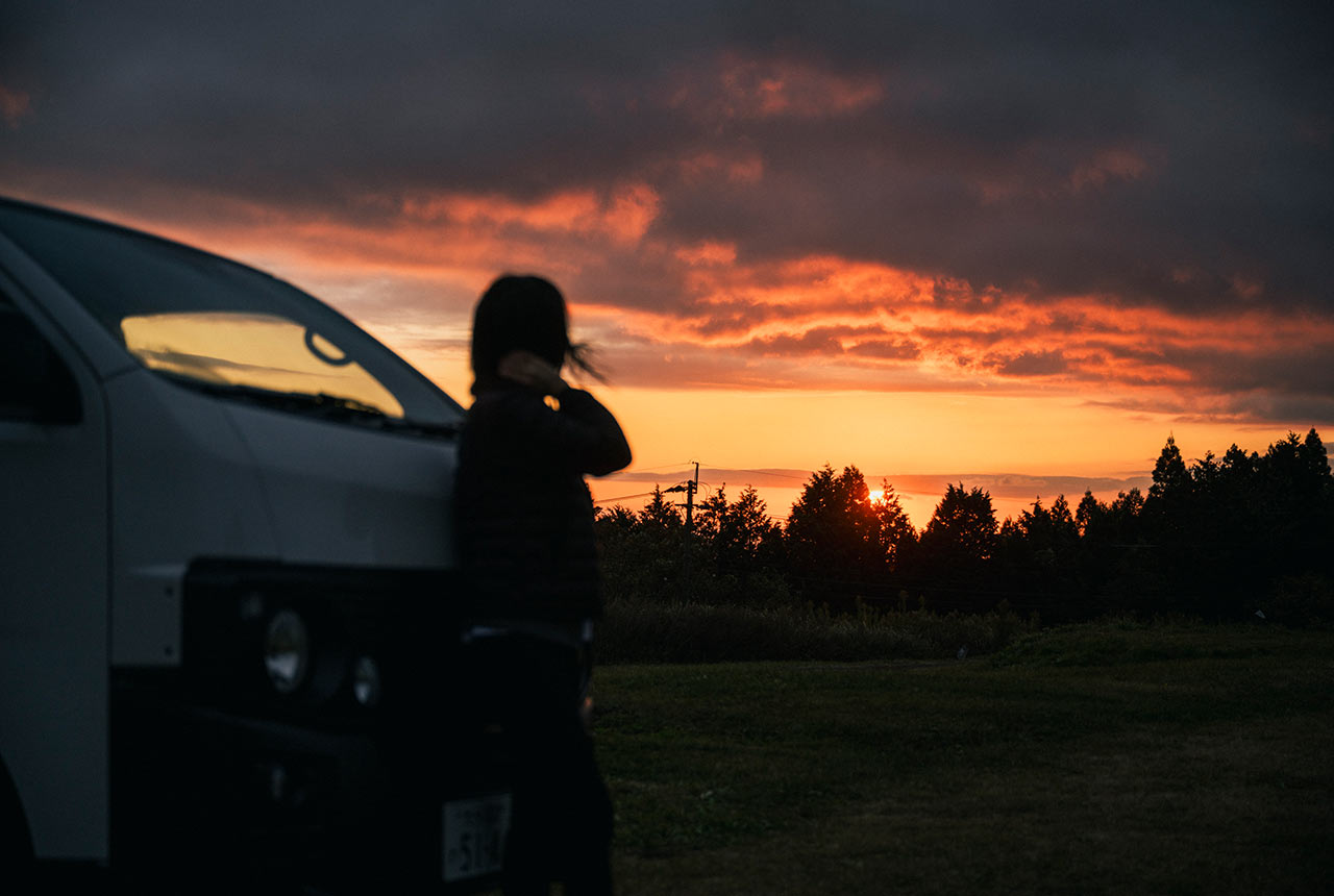 レンタルバンにもたれて日の出を望む女性