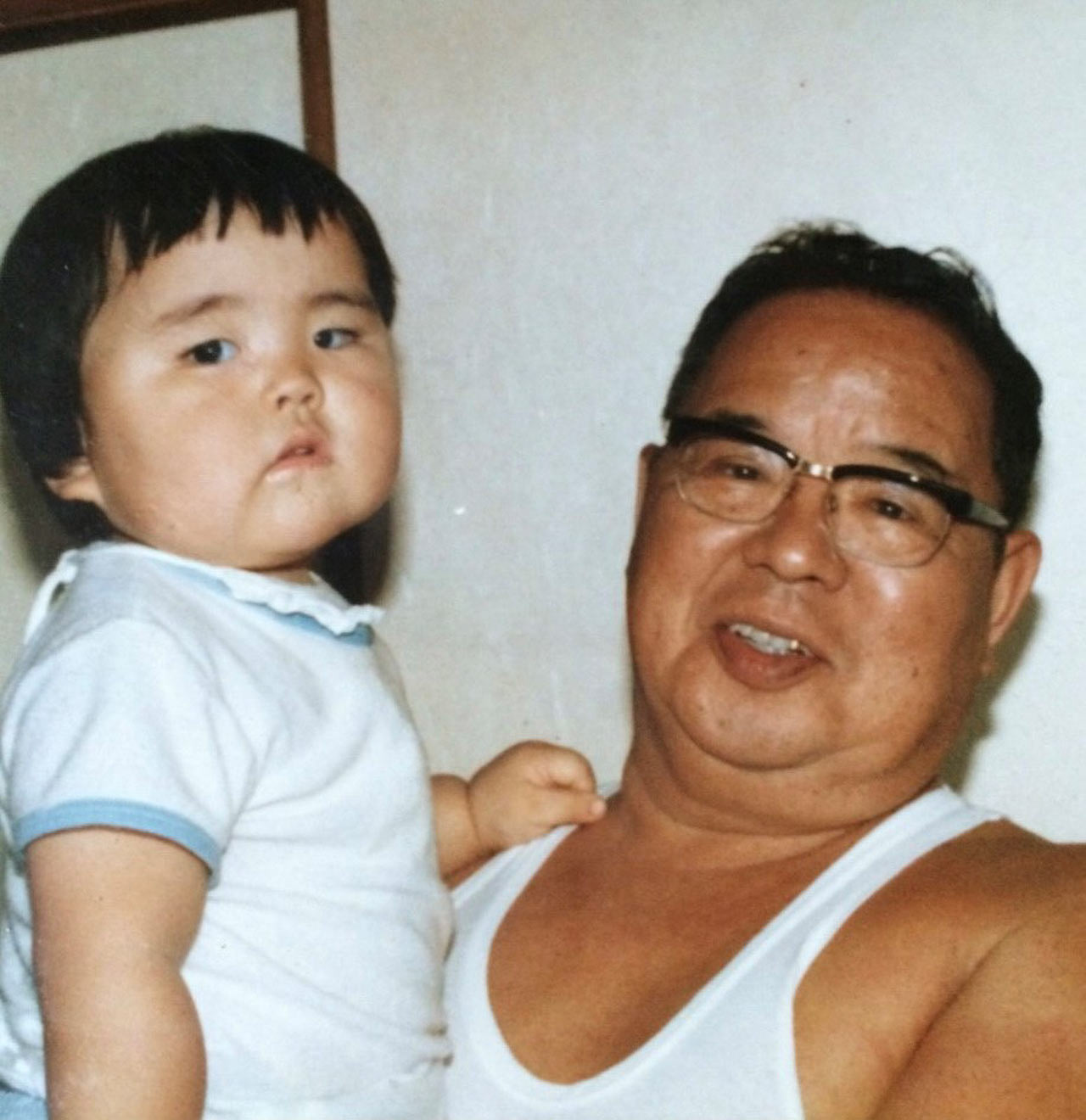 祖父に抱っこされる幼い頃の敦士さんの写真
