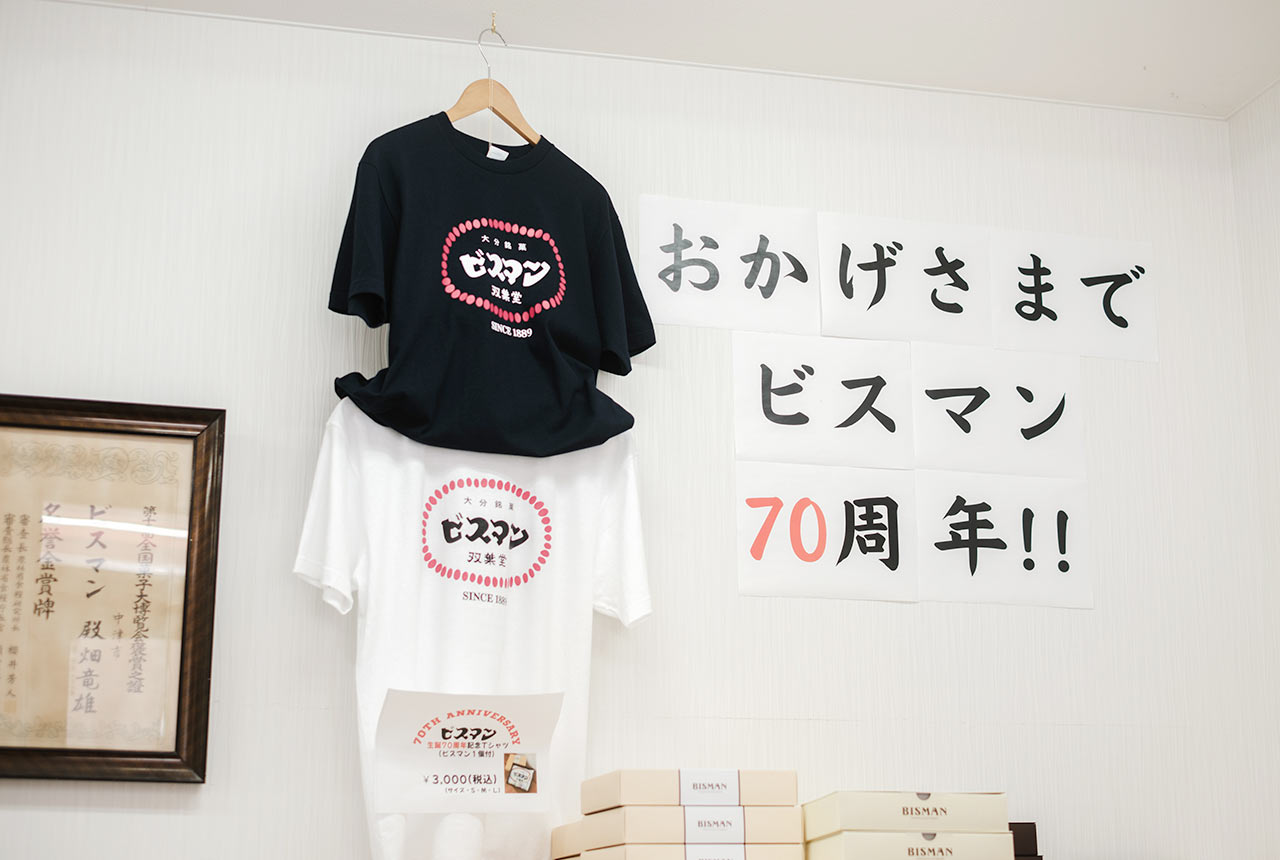 壁に飾られた、白黒２色のオリジナルTシャツと「おかげさまでビスマン70周年!!」の文字