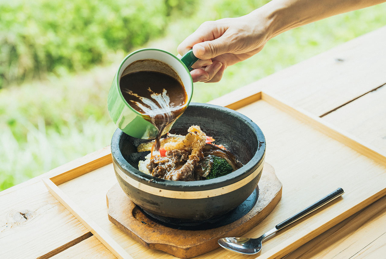 ご飯と具材が入った器にカレーを注いでいる
