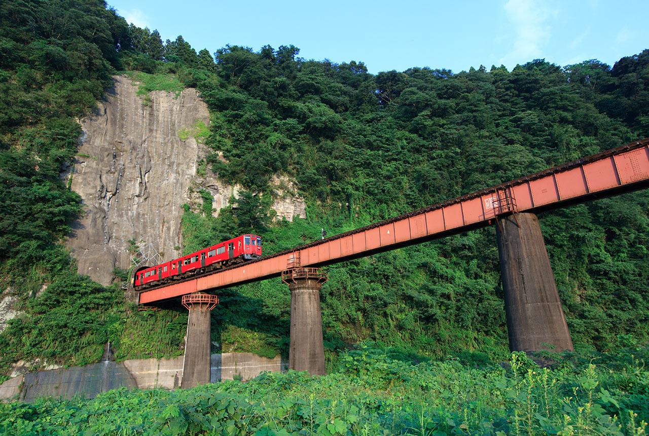 絶壁のトンネルから伸びた鉄橋を走る赤い列車